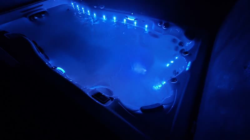 Swim spa lit deep blue, wide view on the deck under the trees
